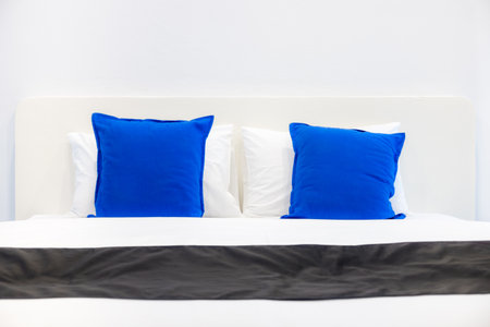 Front view of white pillows and blue cushions on bed in a bedroom. The plain design of romantic light pale room.の写真素材