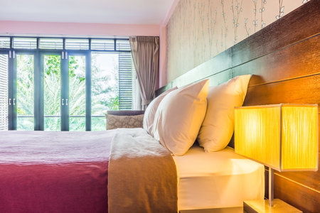 Interior decoration of contemporary bedroom with wide glass balcony doors. It consists of bed, white pillows and modern lamps.の写真素材