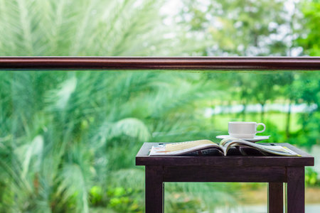 Open magazine and coffee cup on wooden table. They are at balcony near park.の写真素材