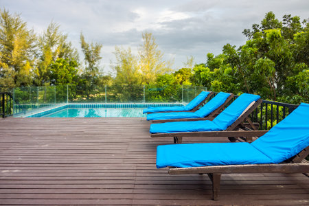 Four sun loungers on wooden decks near swimming pool. The exterior decoration on rooftop for...