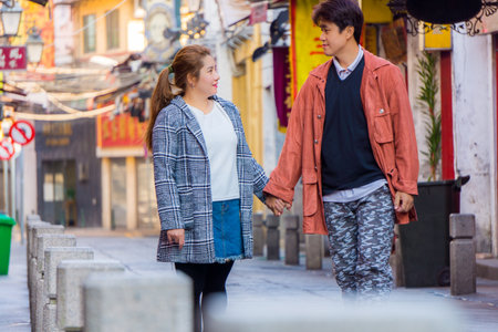Sweet Asian couple holding hands and staring into eyes each other on Happiness Street. This landmark street name is Rua da Felicidade in Macau, China, Asia.の写真素材