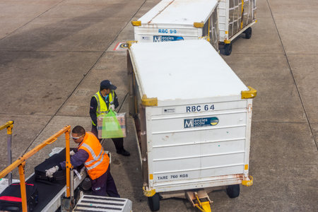 MACAU - JUN 21, 2019: Baggage handlers are lifting and hauling suitcases from airplane. They are working in Macau International Airport, China, Asia.のeditorial素材