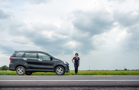 Female tourist standing with arm akimbo in front of her car. It is breaking down at roadside in rural area.の写真素材
