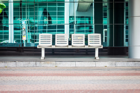 A 4-seat bus waiting bench at a modern bus stop station. The seats are white and are made of metal.の写真素材