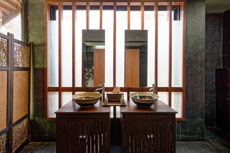 Restroom in traditional Thai charm. A traditional Thai-inspired bathroom showcasing intricate wooden latticework, ceramic sinks, and dark wooden accents, creating a sense of tranquility and cultural richness.の写真素材