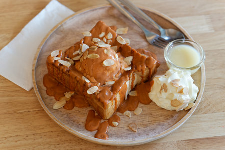 Thai Milk Tea Toast with Ice Cream and Almonds. A dessert featuring thick slices of toast topped with a Thai tea sauce and ice cream. Garnished with sliced almonds, whipped cream and condensed milk.の写真素材