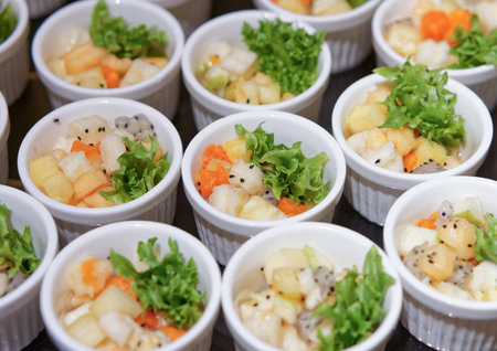 Fresh Fruit Salad in Arranged White Ramekins. The fruit salad includes diced tropical fruits such as dragon fruit, pineapple, papaya, melon, garnished with green lettuce and black sesame seeds.の写真素材