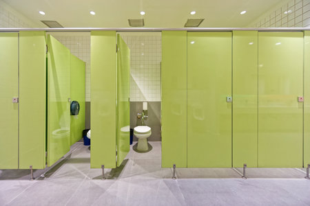 Modern Public Restroom with Green Partition Doors. A clean and well-maintained public restroom featuring bright green partition doors, white tiled walls, tiled floor and white toilet.の写真素材
