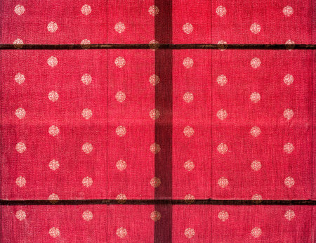 Traditional red textile with gold floral motifs and symmetrical woven pattern. Close-up of fabric with circular flower patterns, showing traditional textile craftsmanship and cultural fabric design.の写真素材