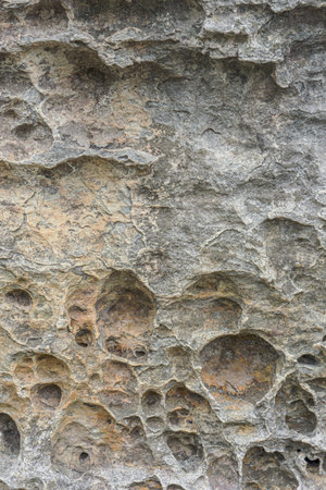 Natural Eroded Stone Texture with Unique Patterns and Pits. Background of ancient weathered rock formation, showcasing intricate patterns, pits, varied earthy tones formed by natural erosion over timeの写真素材