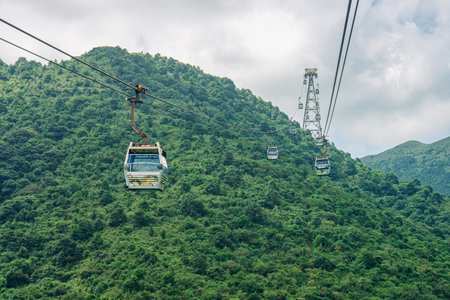 Cable car ascending over lush mountains with a panoramic sky view. Experience a breathtaking expansive vista as the gondola lift ascends majestically over the green, verdant peaks.の写真素材