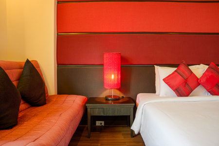 Modern Hotel Bedroom with Red and White Decor. A contemporary hotel room featuring a comfortable bed with white linens, a striking red headboard, and a matching red lamp.の写真素材