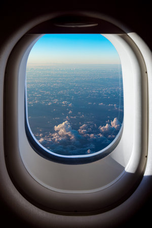 Breathtaking Clouds from an Airplane Window View. A stunning aerial view from airplane window, showcasing vast expanse of fluffy white clouds beneath clear blue sky.の写真素材