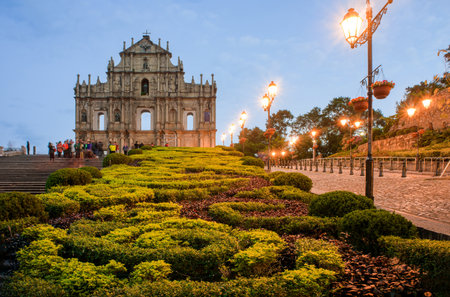 Iconic Ruins of St. Paul's at Dusk, Macau. Facade of Ruins of St. Paul's, beautifully illuminated at dusk, with lush green and red foliage in foreground and glowing street lightsの写真素材
