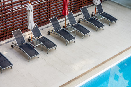 Luxury Poolside View with Gray Sun Loungers and Vibrant Blue Swimming Pool Water. A row of modern...