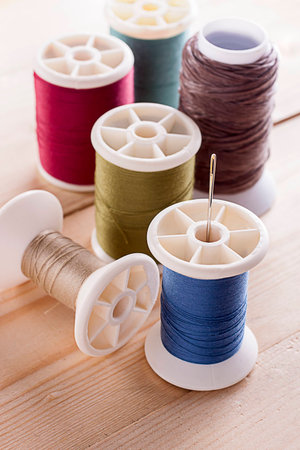 Colorful spool of threads with sewing needles on wooden table 