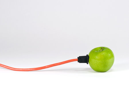 A green apple with an electrical cord plugged into itの写真素材