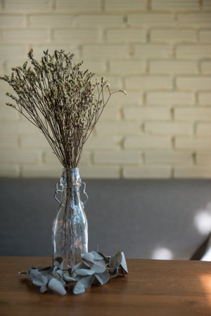 Dried flowers in a clear glass bottle, enhancing the decor on a wooden table with their rustic charm.の写真素材
