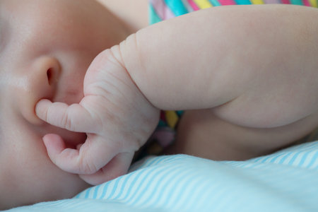 The picture captures a cute moment of a newborn baby attempting to explore by putting a finger in their nose, showcasing their curiosity and early motor skills developmentの写真素材