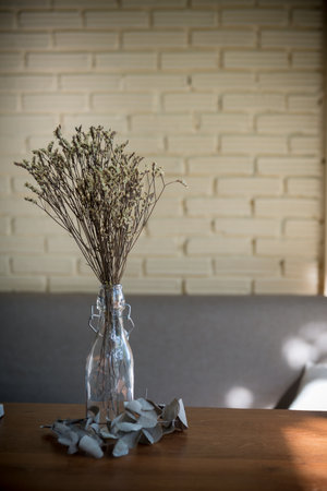 Dried flowers in a clear glass bottle, enhancing the decor on a wooden table with their rustic charm.の写真素材