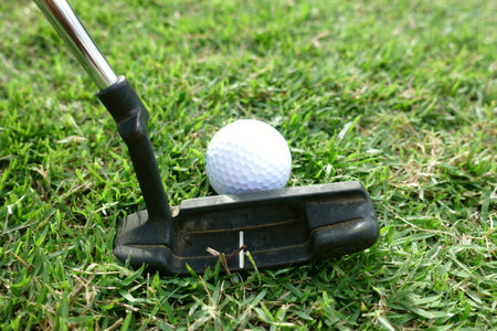 Golf player at the putting green hitting ball into a hole