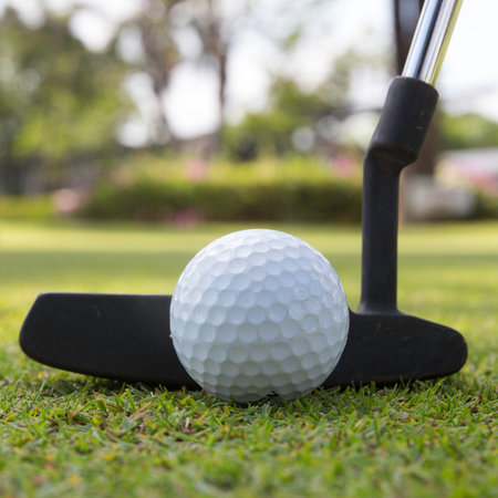 Golf player at the putting green hitting ball into a hole 