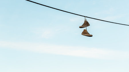 Pair of old shoes or sneakers hanging from a power line by the lacesの写真素材