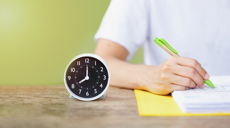 close up of woman hand writing on a paper file beside alarm clock