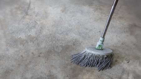 Close-up image of a round mop head cleaning an old, stained concrete floor. The image shows cleaning in progress, with visible texture and cracks on the floor surface, symbolizing cleanliness, maintenance, and hard work.の写真素材