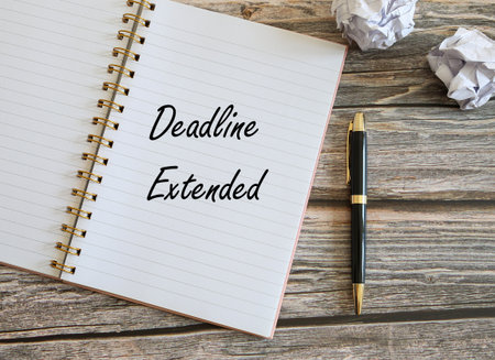 Top view of a notebook and pens with Deadline Extended written on a notebookの写真素材