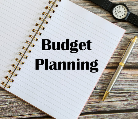 Top view of a pen and a watch with Budget Planning written on a notebook.の写真素材