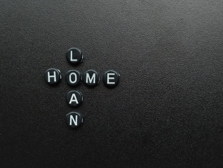 The words "HOME" and "LOAN" are spelled out using letter beads, forming a cross shape on a dark, textured background, representing the financial concept.の写真素材