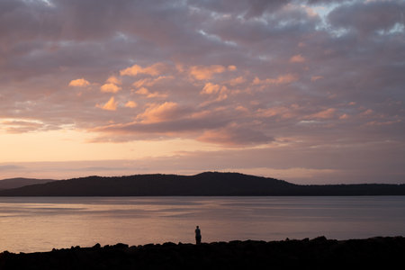 Silhouette of a man standing in front of the sea at sunsetの写真素材