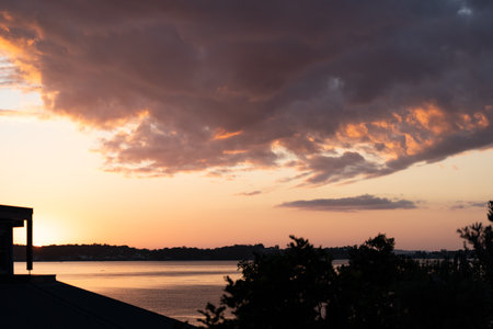 Sunset over the sea with clouds in the sky and silhouette of treesの写真素材