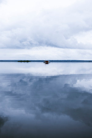 A house floating on the calm sea with a cloudy sky and the forsest in background