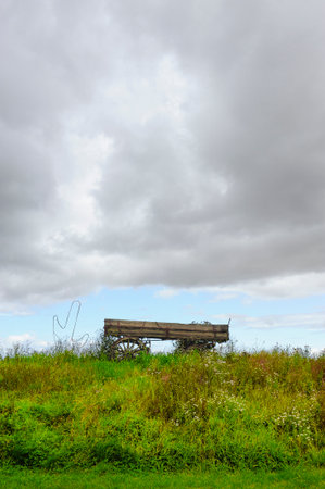 An old wagon standing at a hill with the cloudy sky behindの写真素材