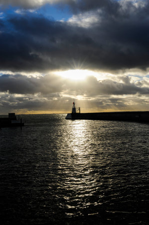 A lighthouse and a sun that tries to press its light through the thick cloudsの写真素材