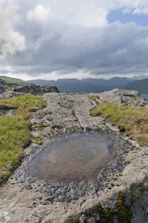 Small puddle in a rock with mountains in the background and a dramatic skyの写真素材