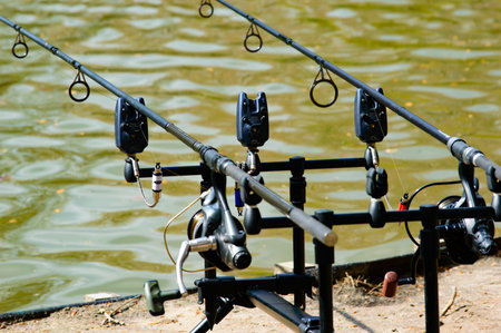 Two fishing rods with attached lines and reels in a rod holder overlooking the calm water of a freshwater lake in a close up viewの写真素材