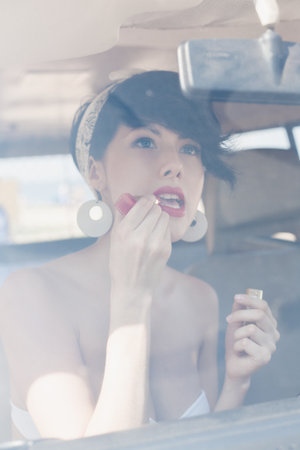 woman looking in rear view mirror and putting make up in carの写真素材