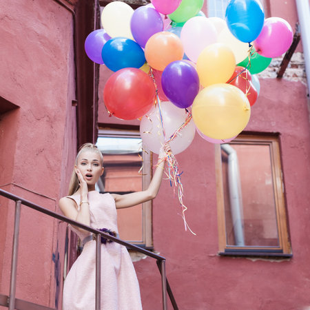 young woman with colorful balloons surprised on a street - outdoorsの写真素材