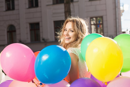 Happy young woman with colorful latex balloons keeping her dress, urban scene, outdoorsの写真素材