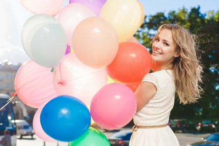 Happy young woman with colorful latex balloons keeping her dress, urban scene, outdoorsの写真素材