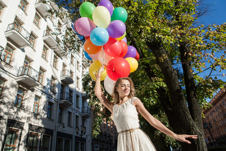 Happy young woman with colorful latex balloons keeping her dress, urban scene, outdoorsの写真素材