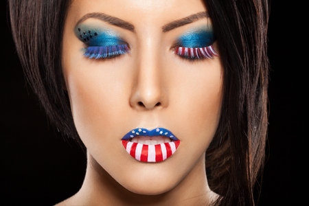 Woman beautiful face with perfect makeup on black backround. on the lips and eyes painted an American flagの写真素材