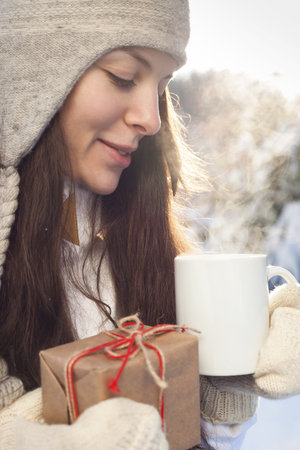 oman drinking tea and holding a gift in hand on a background of a winter landscape, outdoorsの写真素材