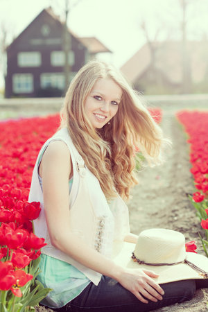 beautiful woman with hat in her hands on the meadow with red flowers tulips, outdoorsの写真素材