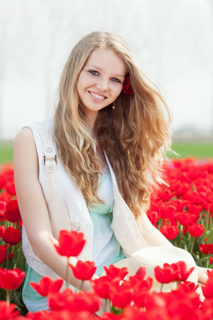 happy young woman with hat on the meadow with red flowers tulips, outdoorsの写真素材