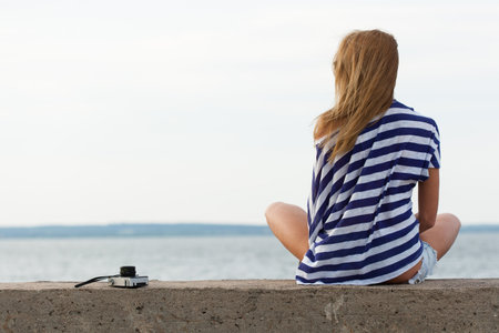Young woman with old camera sitting on pier on the sea background. Outdoor, lifestyleの写真素材