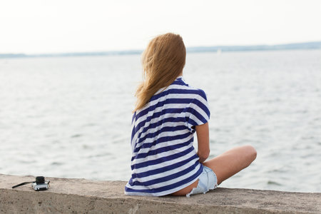 Young woman with old camera sitting on the sea background. Outdoor, lifestyleの写真素材